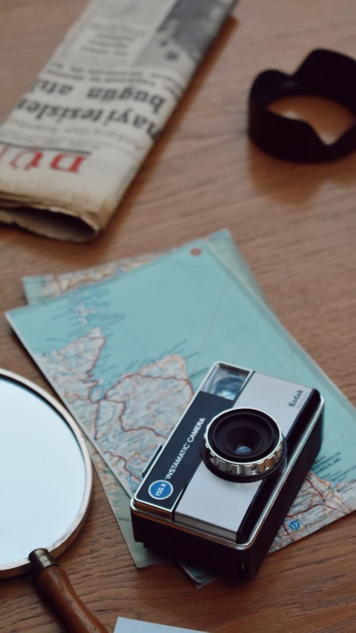 gallery-04 A vintage camera, maps, and newspaper on a wooden table create a nostalgic travel vibe.